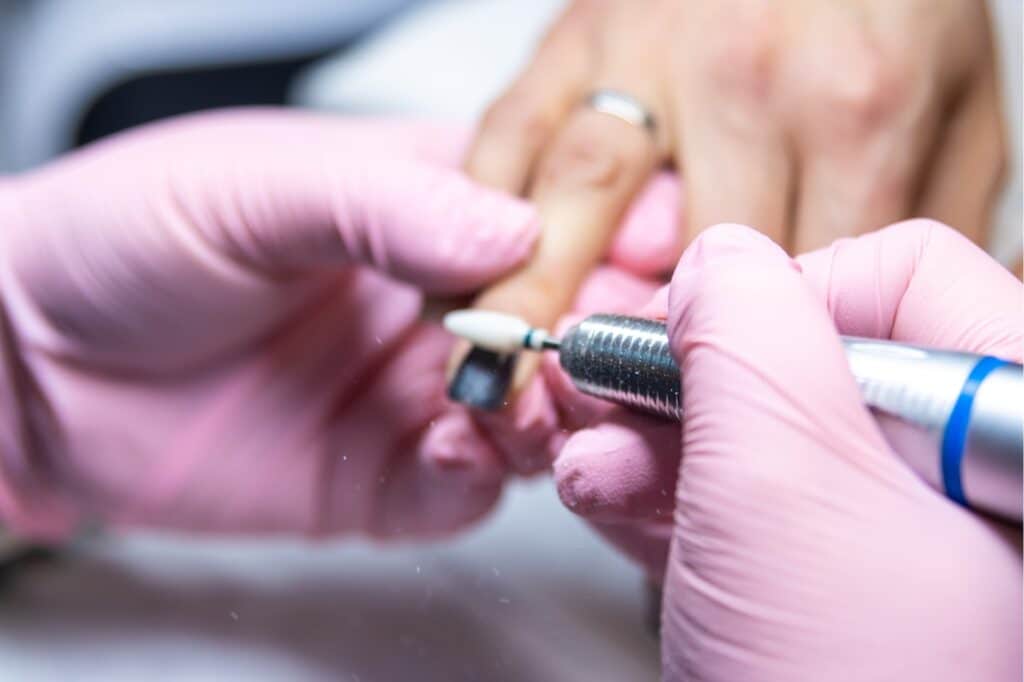 nail technician wearing pink gloves drilling the nails of customer who has ring on